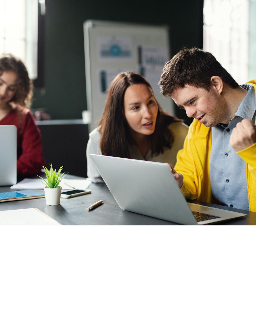 Ein junger Mann im Rollstuhl sitzt vor einem Laptop. Eine Frau sitzt rechts von ihm und sie sind im Gepräch